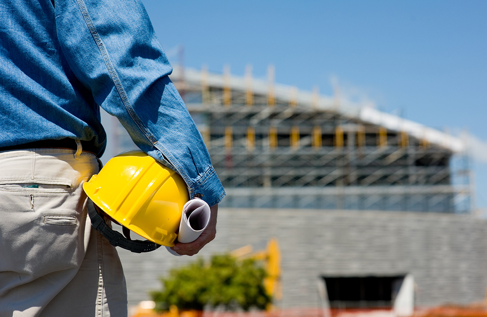 Man on construction site holding helmet for tower crane